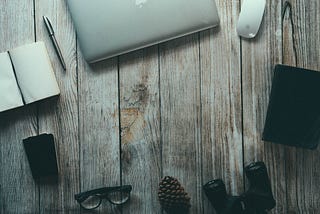 A laptop, glasses, pen, and notebooks laying on a wooden desk