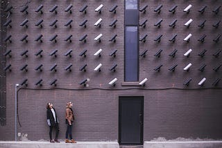 Two women underneath a wall of surveillance cameras having their privacy threatened by technology