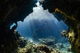 Two divers swimming past a cave under the sea