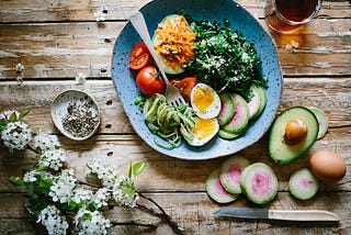 A healthy meal featuring fruits and veggies on a blue plate, situated on a wooden surface.