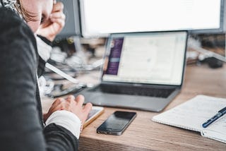 A person typing on their phone in front of their laptop