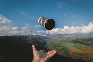 A hand throwing a cup into the air with a scenic background of mountains and grasslands.