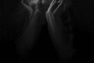 A double exposure, black and white image of a woman screaming while holding her face.