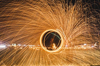 A spray of light spins out from a central circle, behind which is a city scape at night.