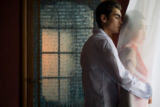 man hugging woman behind sheer curtain