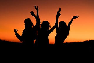 three women dancing in with an orange sky in the background