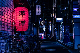 At night, a back alley in downtown Tokyo is lit by business signs