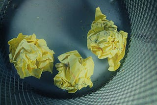 three crumpled up pieces of yellow notebook paper in a waste basket