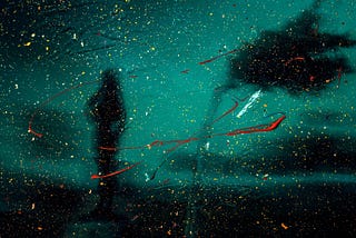 A hazy silhouette of a woman walking towards a tree that is blowing in the wind.