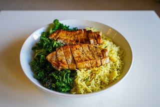 A bowl of kale and rice with sliced chicken laid across the top