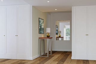 Image of an entryway featuring lagre white built-in closets and a niche with a table and lamp.