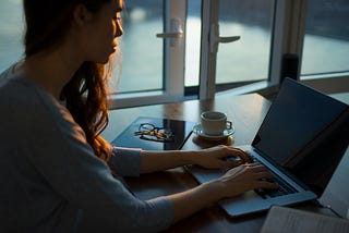 Color photo close up of woman working on a laptop in dim light, indicating “back to work after baby”