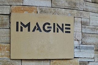 black text with the word imagine on a piece of slate, on a slate wall.