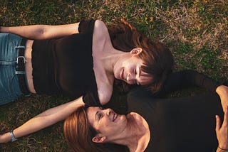 Mother and daughter laying on the grass together looking at eachother