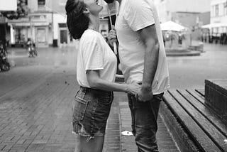 Man and woman outside kissing in the rain.