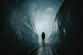 A dark figure stands in a tunnel covered in ice.