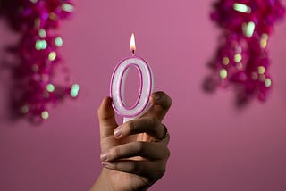 Girl’s hand holding a lit candle shaped as a zero with glittery shapes in the background