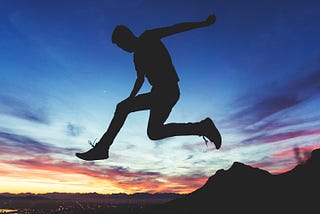 A shadow of a figure leaps across a horizon of a rising sun.