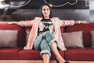 Woman sitting on a red couch arms wide open to the sides and legs crossed looking confident.