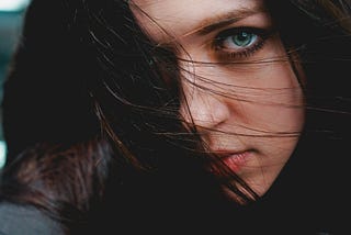 Young woman with green eyes and dark hair blowing across her face