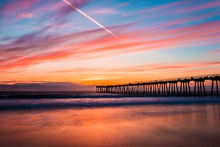 A view of Hermosa Beach during a sunset with a bridge blocking the view.