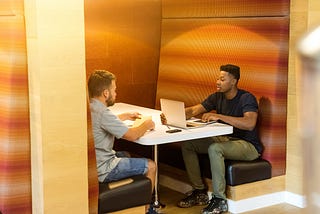 Two men sitting across the desk in a conference room, talking to each other