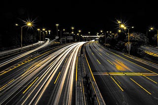 A photo of multiple highway lanes at night. The yellow lines and street signs are lit against a grey and black background. The highway lacks cars indicating an inward journey, not a physical one.