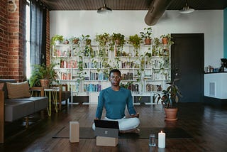 A man practicing meditation while using his laptop and tablet which is placed in front of him