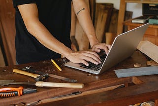 A person typing on a laptop with a bunch of tools around it.