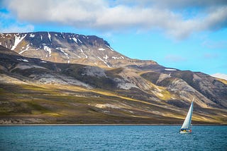 A sailboat on the water on a partly cloudy day in front of a mountain.