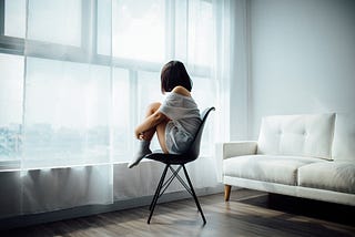 person curled up on a chair looking out a window