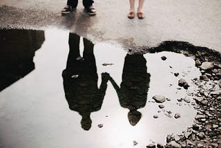 A couple reflected upside down in a puddle of water, holding hands.