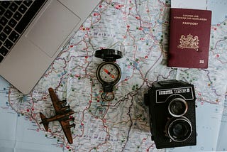 A photo array of pre-digial travel items, including a map, a camera and a compass.