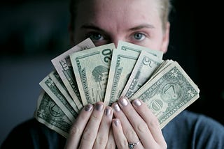 A woman holds up a fan of banknotes close to her face