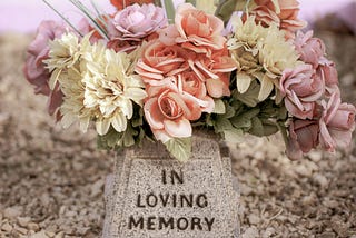 A memorial stone that reads “In Loving Memory” surrounded by pink and white flowers