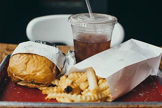 Photo of a fast-food hamburger, french fries, and a cola in a plastic cup