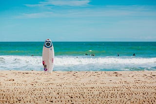 A surfboard standing vertically on a beach with emerald-green water
