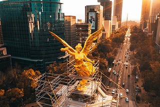 Gold statue of a winged woman, surrounded by scaffolding and above a busy freeway
