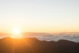 A landscape with the sun rising against a light blue sky..