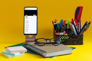 A notebook, sticky notes, pens, glasses, and an app