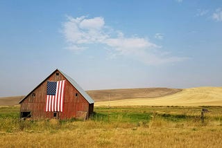 A farm with its barn displaying a large American flag.
