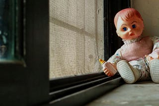 a baby doll, clutching a toy milk bottle, sat on a window sill