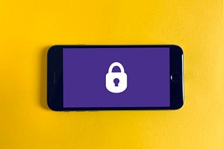 A smartphone rested on a yellow background. On the smartphone screen is a white lock icon resting on a blue background.
