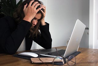 A woman sitting in front of the laptop with head between both hands.