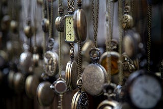 A display of dozens of older pocket watches hang from a wall, filling the frame.