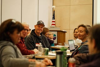 A group of Kickstart Your Podcast students sharing their podcast ideas at a workshop table, looking excited and engaged.