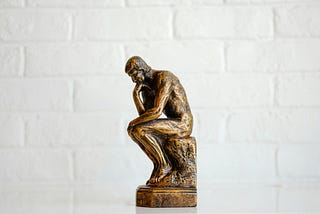 a small bronze image of the statue,“The Thinker” against a white brick background