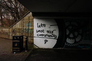 A picture of a street under a bridge where the graffiti says, “Let’s love our community”