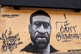 Grey-scale mural of George Floyd on a plywood covered storefront with the words “I Can’t Breathe!” “Stand United” and “Stop the Violence”