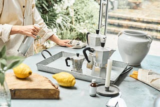 women cleaning table with cleaner in one hand and cloth in another.